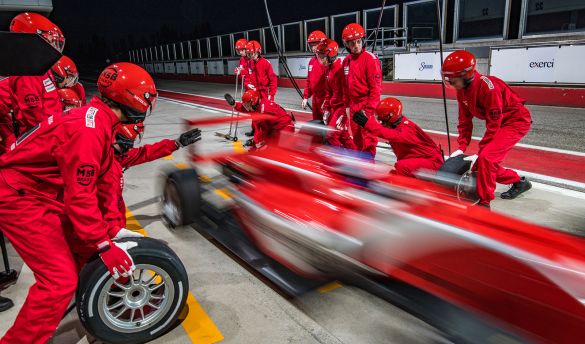 Rennteam in roten Uniformen wechseln Reifen eines roten Rennwagens während Boxenstopps