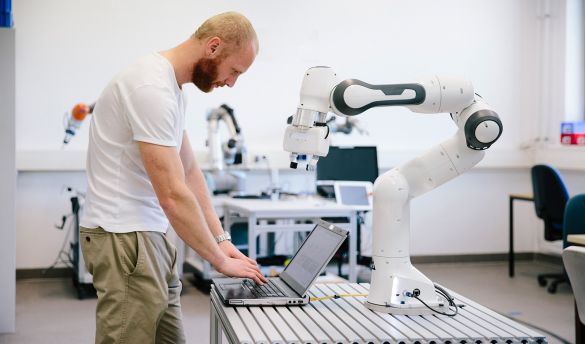 Mann steh vor einem Laptop und einen Roboterarm