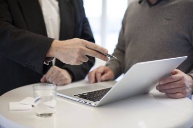 Zwei Personen stehen vor einem Laptop und sprechen über den dort angezeigten Inhalt